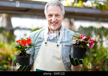 Portrait of a smiling greenhouse worker holding flower pots Stock Photo