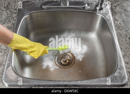 Female hand in yellow glove cleaning the kitchen sink.