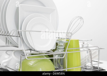 Green and white dishes drying on metal dish rack. White background. Stock Photo