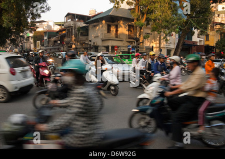 Horizontal cityscape of a busy crossroads in Hanoi with lots of mopeds driving in all directions during rush hour. Stock Photo