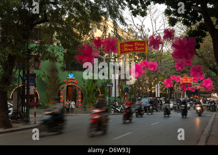 Horizontal cityscape of a Tràng Thi street in Hanoi with lots of mopeds driving along during rush hour. Stock Photo