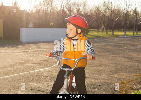 Handsome happy little boy out riding his bicycle standing in a rural road in his helmet and high visibility jacket smiling cheerfully in the sunshine. Stock Photo