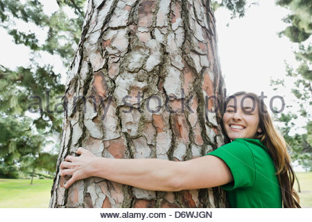 Side view of happy young woman hugging tree in park