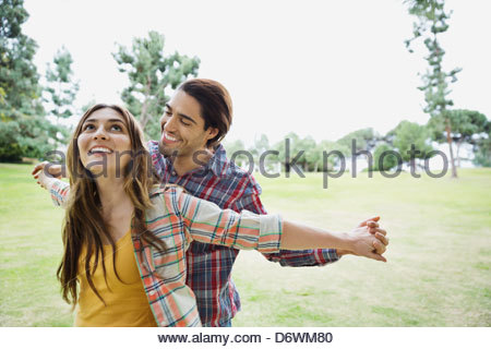 Happy young couple with arms outstretched holding hands in park