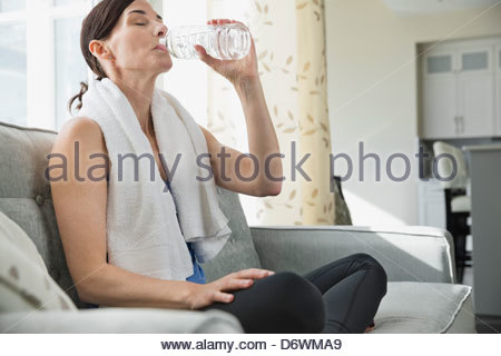 Mature woman drinking water from bottle on sofa