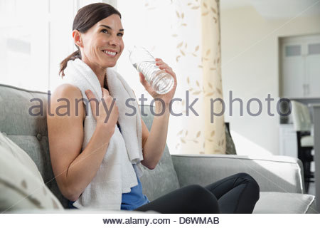 Happy mature woman holding water bottle while looking away on sofa