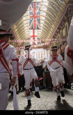 Morris man and lunchtime drinkers gather in Leadenhall Market on St George's Day, when 'Englishmen' celebrate their patron saint. Wearing white uniforms they jig their traditional dance, a form of English folk dance accompanied by accordion and pipes. It is based on rhythmic stepping and the execution of choreographed figures by a group of dancers. Implements such as sticks, swords, and handkerchiefs may also be wielded by the dancers. (more in Description) .. Stock Photo