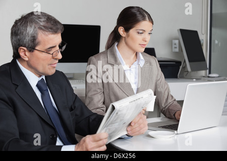 Business woman working with laptop and man reading newspaper in the office Stock Photo