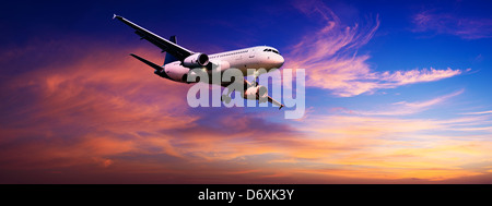 Jet is maneuvering for landing in a sunset sky. Panoramic composition. Stock Photo