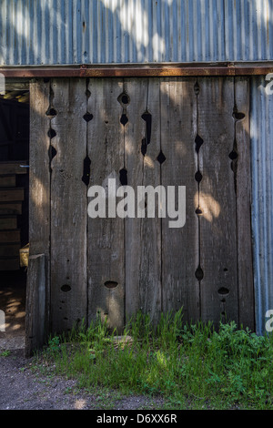 A detail of a well worn wooden barn door with unusual shaped holes in the wood attached to a corrugated steel exterior. Stock Photo