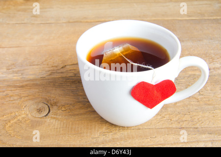 White cup of tea with red heart shaped label on teabag on wooden background (surface). Love and care concept. Stock Photo