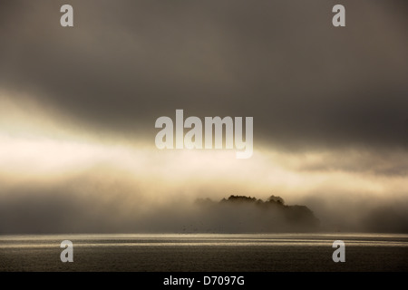 Island in front off coast covered with fog and clouds Stock Photo