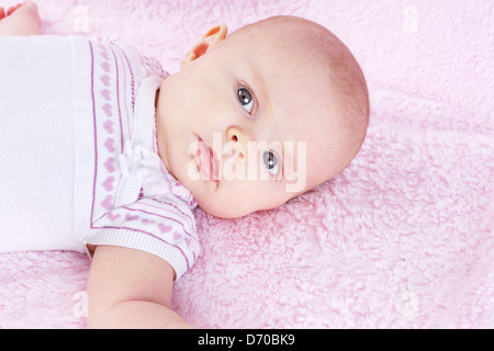 Portrait of newborn baby girl looking at camera, laying on pink blanket Stock Photo