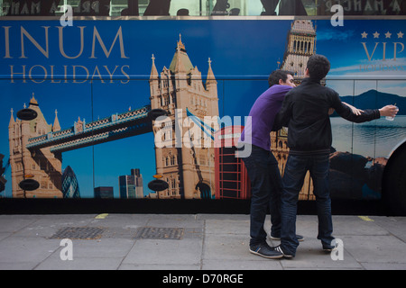 A parked tour coach for Platinum Holidays features famous London landmarks as two boys playfully fight over a drink. On the side of the bus are the places that attract visitors to Britain's capital: Tower Bridge; Big Ben and a red telephone box. Stock Photo