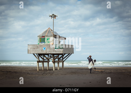 A surfer stands beside the lifeguards' lookout tower on Bethells Beach (Te Henga), on Auckland's West Coast, New Zealand. Stock Photo