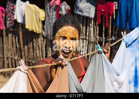 Local girl, face applied with clay as sunblock, hanging laundry on cloth line, Morondava, Madagascar Stock Photo
