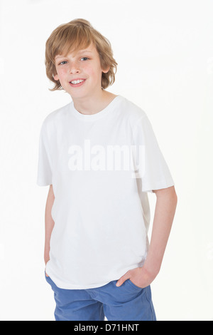 White background studio photograph of young happy boy smiling hands in pockets wearing blue denim jeans and white T-shirt Stock Photo