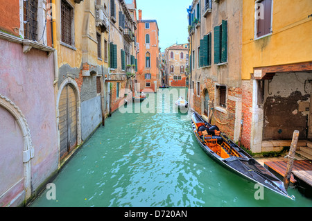 Gondola floats on small canal among old colorful houses in Venice, Italy. Stock Photo
