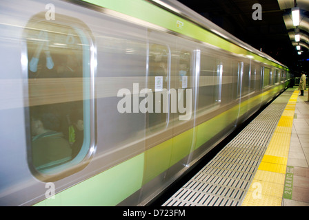 A lone commuter waits for his train at a subway station in Tokyo, Japan, as other passengers whiz by on the green line. Stock Photo