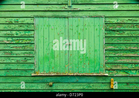 A shuttered window of an old wooden shed with peeling paint. Stock Photo