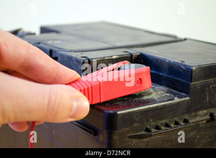closeup of hand plug car automobile battery charger red clamp on accumulator plus. Stock Photo