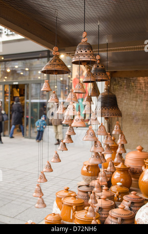 clay pots and hanging bells wares sold in outside store shop market and people walk in city street. Stock Photo