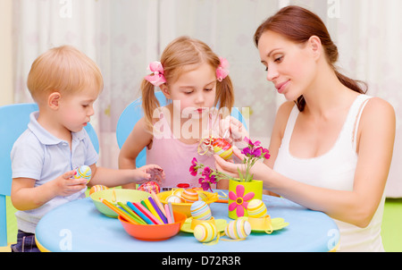 Two little kids with young teacher paint Easter eggs, art lesson, interacting children in daycare, Christian holiday concept Stock Photo