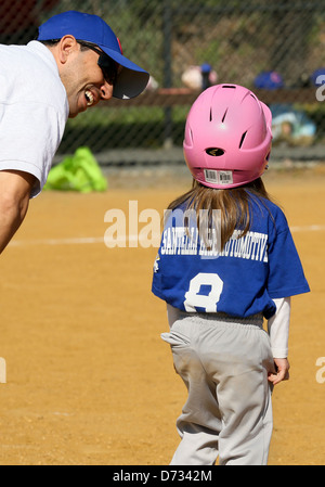A little girl baseball player on first base getting encouragement from her coach. Stock Photo