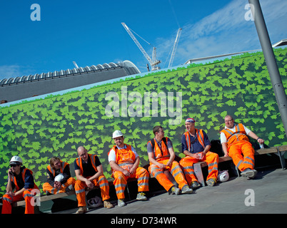 Seven workers wearing orange high visibilty saftey clothing taking a break on Kings Boulevard, Kings Cross, London Stock Photo