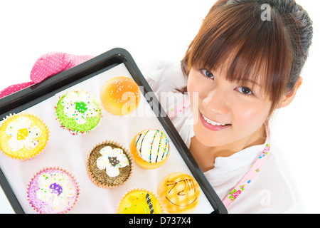 Young Asian woman baking bread and cupcakes, wearing apron and gloves holding tray isolated on white. Stock Photo