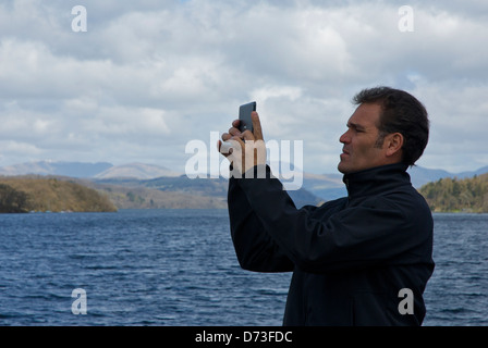 Man using iPad to take photographs, on passenger steamer on Lake Windermere, Lake District National Park, Cumbria, England UK