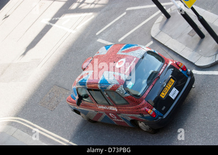 A traditional London black cab wrapped in a Vodafone advertisement styled with the Union Jack flag—merging national pride with brand visibility in central London, UK. Stock Photo