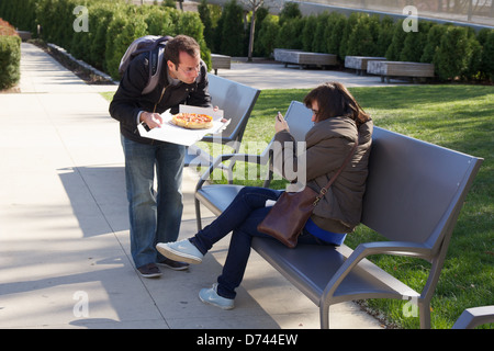 Man tempts woman with pizza while she texts on smart phone. Millennium Park Chicago Stock Photo