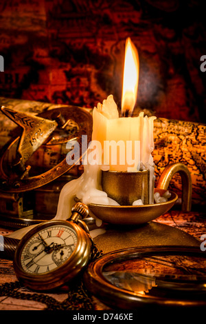 Vintage compass, pocket watch lie on an old ancient map with a lit candle Stock Photo