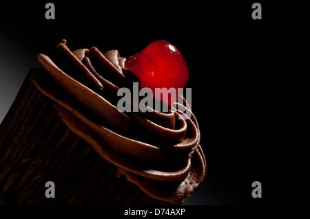 Chocolate cupcake decorated with chocolate frosting and glacé cherry, on black background Stock Photo