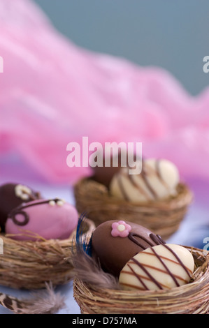 Set of three paired mini chocolate Easter eggs set in natural straw nests decorated with real feathers Stock Photo