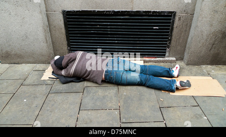 Man prostrate asleep (maybe drunk or hungover) passed out on pavement by heating vent to keep warm Swansea Wales UK KATHY DEWITT Stock Photo