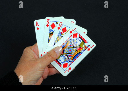 Woman holding playing cards, Ace, King, Queen and Jack of Diamonds against a black background. Stock Photo