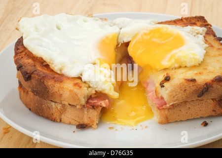 A toasted and cut open Croque Madame sandwich with melted cheese and ham topped with a fried egg. Stock Photo