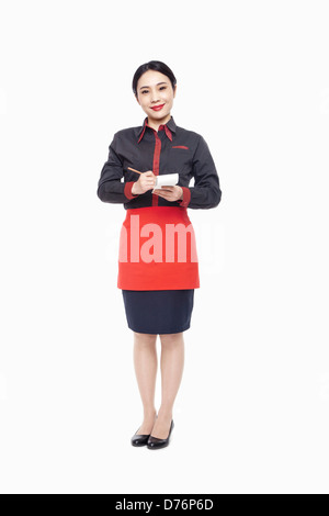 Young Waitress writing order on note pad, smiling, studio shot Stock Photo