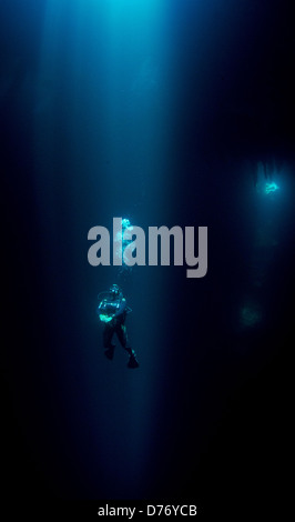 Mexico Puerto Morelos Female scuba diver descending in cenote sun beams around her Stock Photo