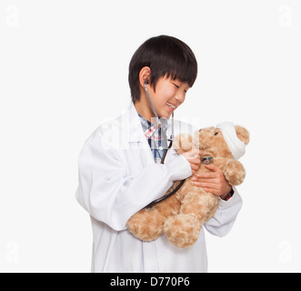 Boy dressed up as doctor checking teddy bear's vital signs Stock Photo