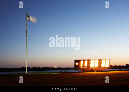 Launch countdown clock American flag Kennedy Space Center Press Site looking toward launch complex 39A illuminated in distance Stock Photo