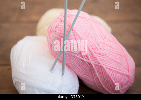 Three balls of wool with a set of knitting needles placed through one ball Stock Photo