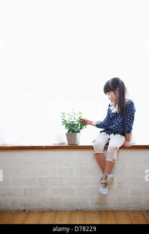 a girl sitting next to a plant in a vase Stock Photo