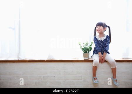 a girl sitting next to a plant in a vase Stock Photo
