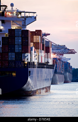 container cargo ships docked in port - three huge freighters at harbor terminal during sunset Stock Photo