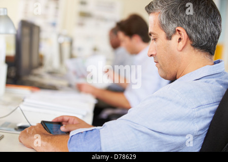 Man Using Mobile Phone At Desk In Busy Creative Office Stock Photo