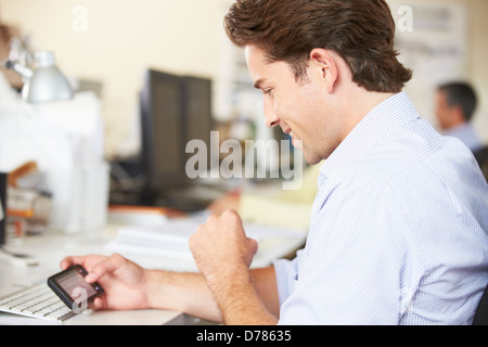 Man Using Mobile Phone At Desk In Busy Creative Office Stock Photo