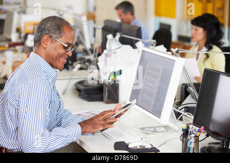 Man Using Digital Tablet In Busy Creative Office Stock Photo